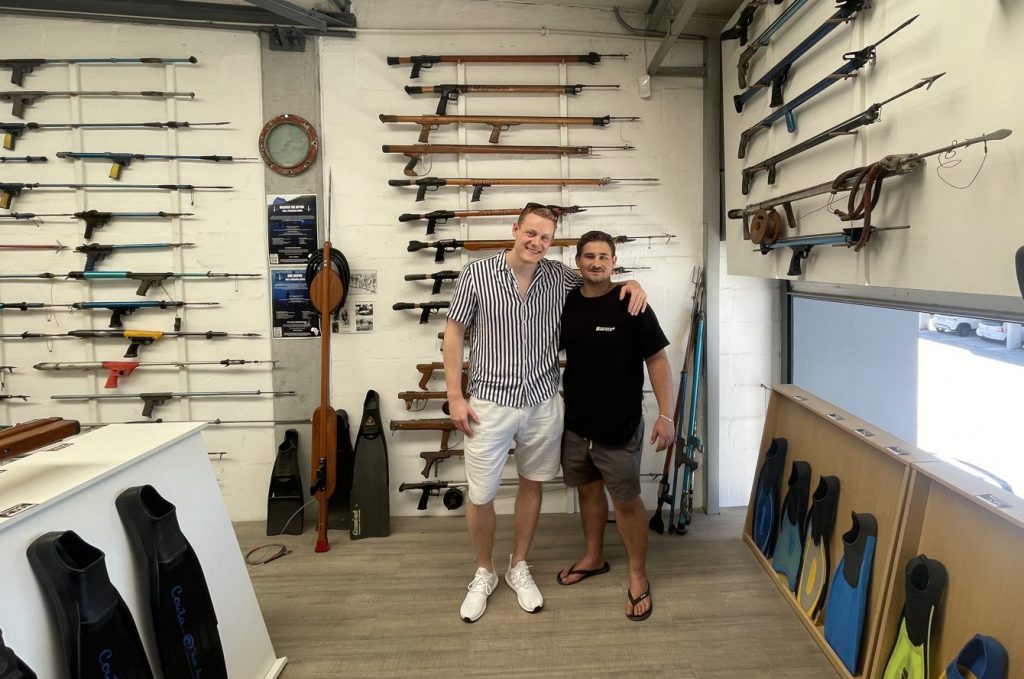 Björn from Spearzen with Jeandre at Rabitech, standing in front of the shop's vintage speargun collection